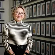 Portrait of a C.C.JENSEN human resources team member standing in front of a wall of framed employee photos.