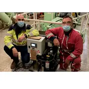 Two service technicians posing beside a CJC® Desorber unit in a vessel engine room.