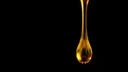 Golden drop of oil suspended against a black background.
