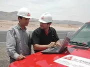 Two engineers wearing safety helmets reviewing information on a laptop beside a service vehicle at an industrial site.
