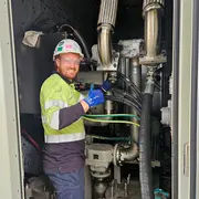 On-site technician inspecting and servicing industrial piping and filtration equipment inside a plant cabinet.
