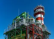 Industrial steam turbine facility with piping and chimney illustrating electrohydraulic control (EHC) systems in power generation.
